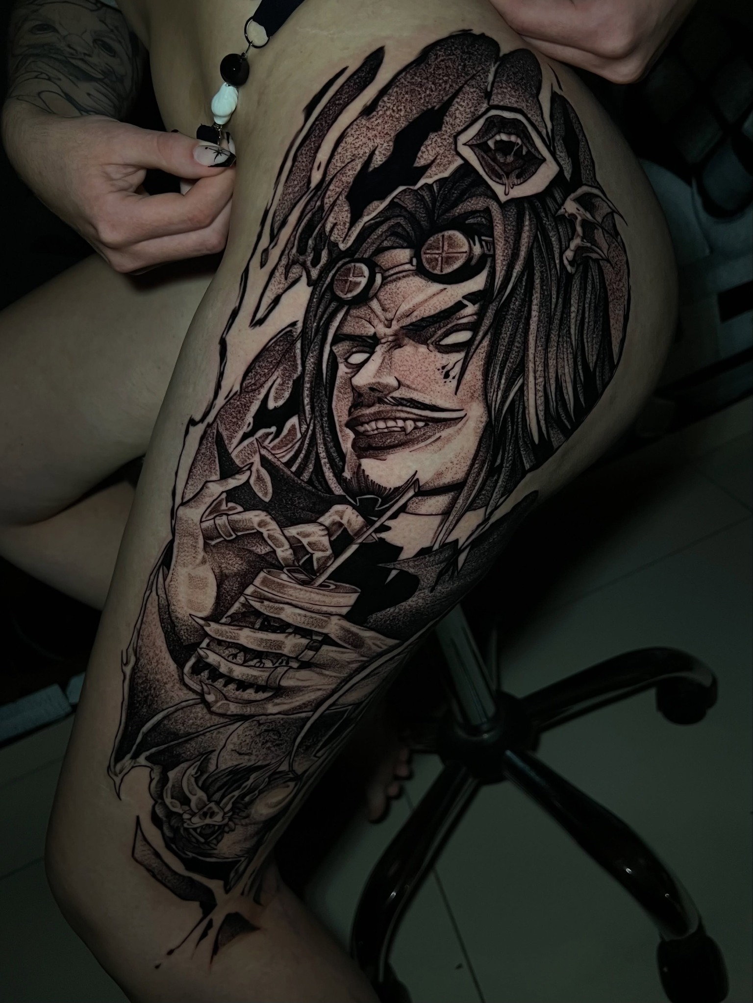 Tatuagem de personagem com chapéu, óculos e elementos de caveira na coxa