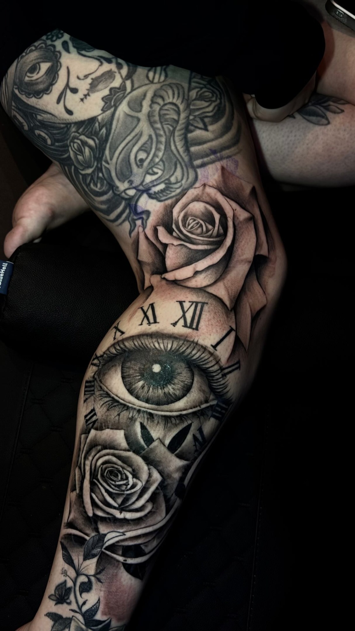 Olho realista com números romanos e rosas em uma tatuagem no braço